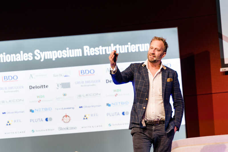 Symp_Vortrag_Nick_Sohnemann | © FH Kufstein Tirol Ein Vortragender hält eine Präsentation im Veranstaltungsraum der FH Kufstein Tirol. Hinter ihm befindet sich eine Wand mit Sponsoring-Logos. | © FH Kufstein Tirol