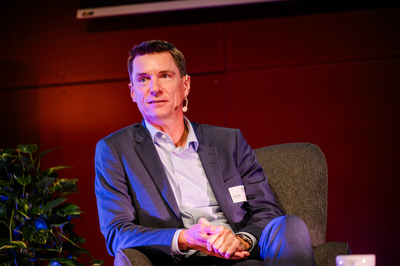 Symp_Vortrag_Jäde | © FH Kufstein Tirol Ein Vortragender des Internationalen Symposiums zur Restrukturierung sitzt auf einem Stuhl auf der Bühne und hält eine Präsentation. | © FH Kufstein Tirol
