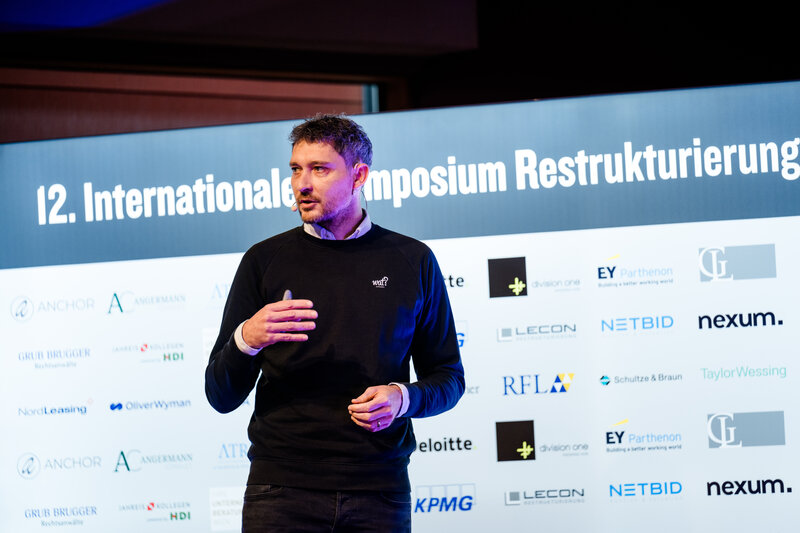 Symp_Vortrag_Lammers | © FH Kufstein Tirol Ein Vortragender hält eine Präsentation im Veranstaltungsraum der FH Kufstein Tirol. Hinter ihm befindet sich eine Wand mit Sponsoring-Logos. | © FH Kufstein Tirol