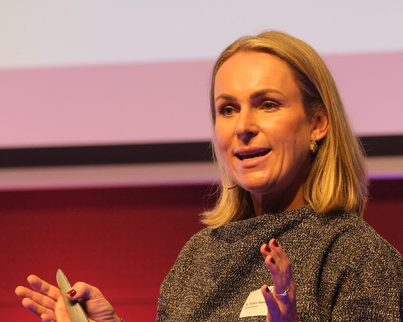 Kristin Nagel als Speakerin beim 14. Internationalen Symposium Restrukturierung Kristin Nagel als Speakerin auf der hell beleuchteten Bühne beim 14. Internationalen Symposium Restrukturierung